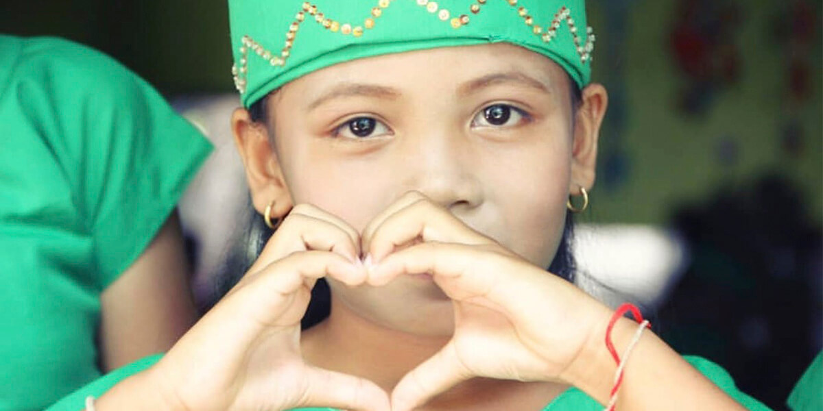Pequeña alumna de la escuela la Llar d'infants del Món Camboya, haciendo la forma de un corazón con las manos.